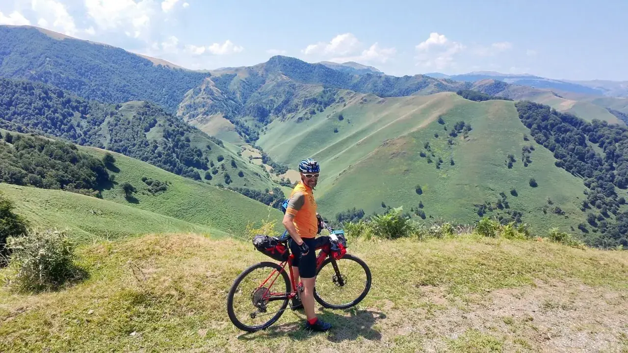 Ciclista con su bicicleta de gravel en un paisaje montañoso verde, disfrutando de la ruta transpirenaica.