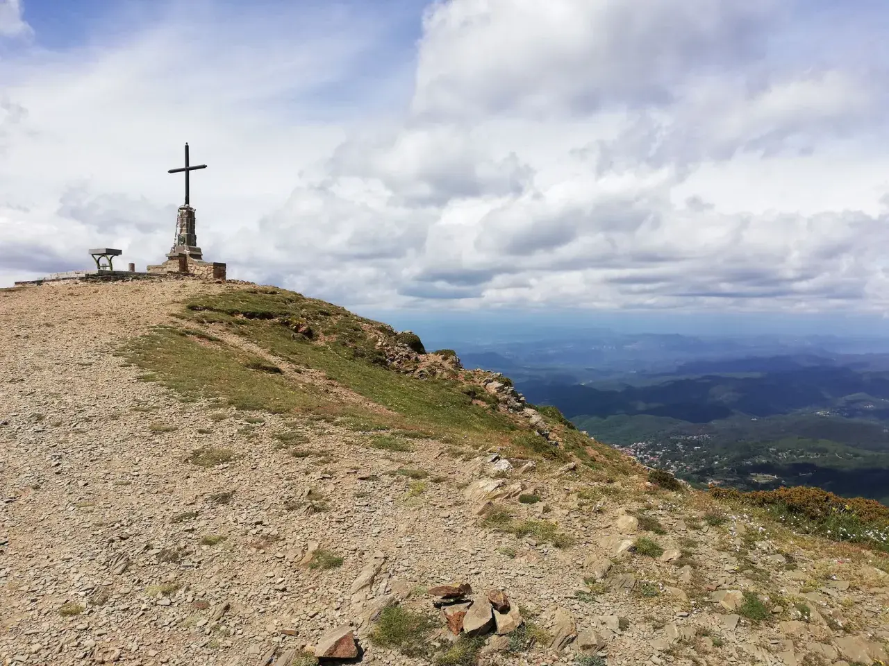 Cima de montaña con cruz y banco, ideal para **rutes per osona**. Paisaje de valles y nubes.