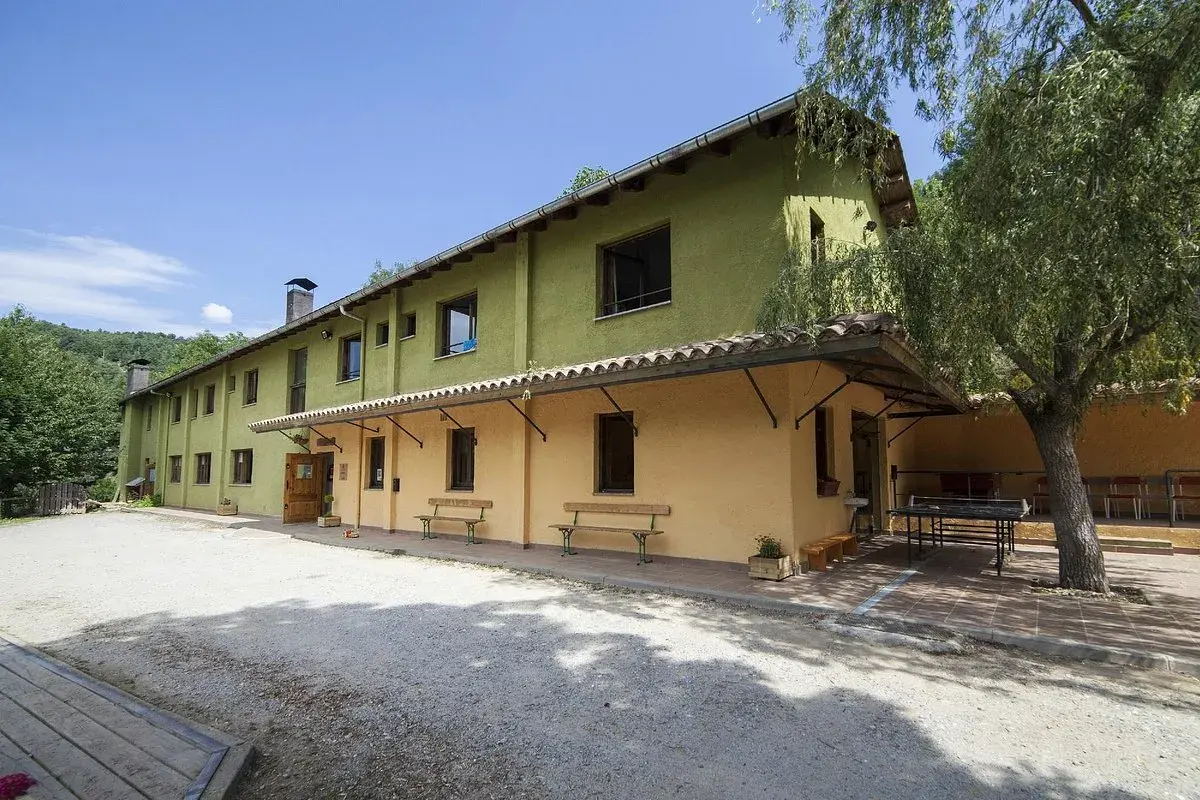 Edifici verd i groc amb taules de ping-pong i bancs a l'exterior. Un lloc ideal per a un refugi cap del rec.