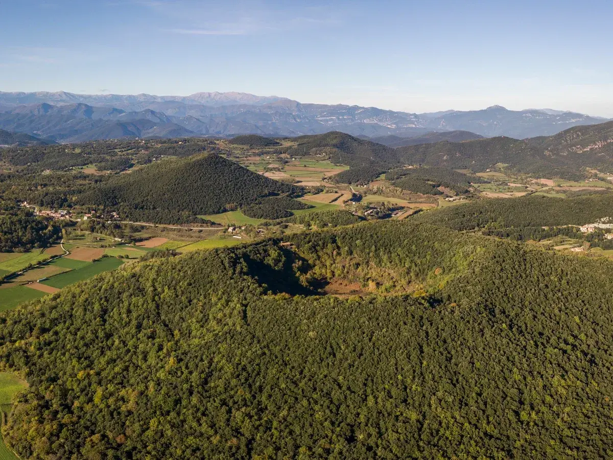Paisaje aéreo de los volcanes de la Garrotxa, con conos volcánicos cubiertos de vegetación y un cráter visible.