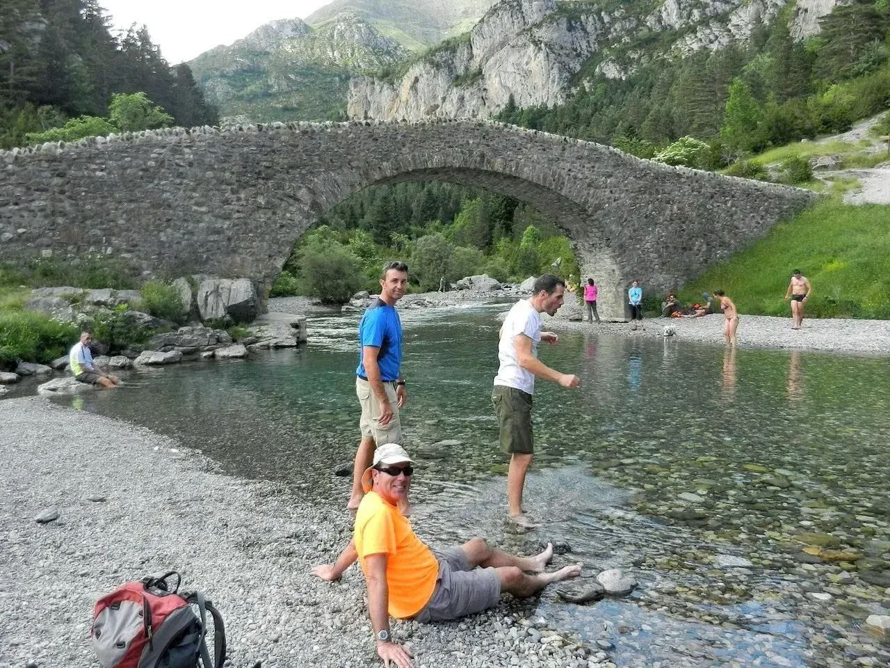 Gente disfrutando del río bajo el puente de piedra en Bujaruelo, con vistas al Taillón.