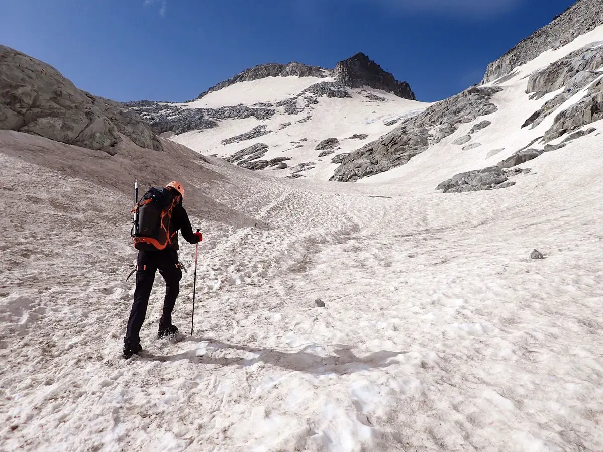 Alpinista asciende por una ladera nevada hacia el pico Aneto, con el cielo azul brillante.