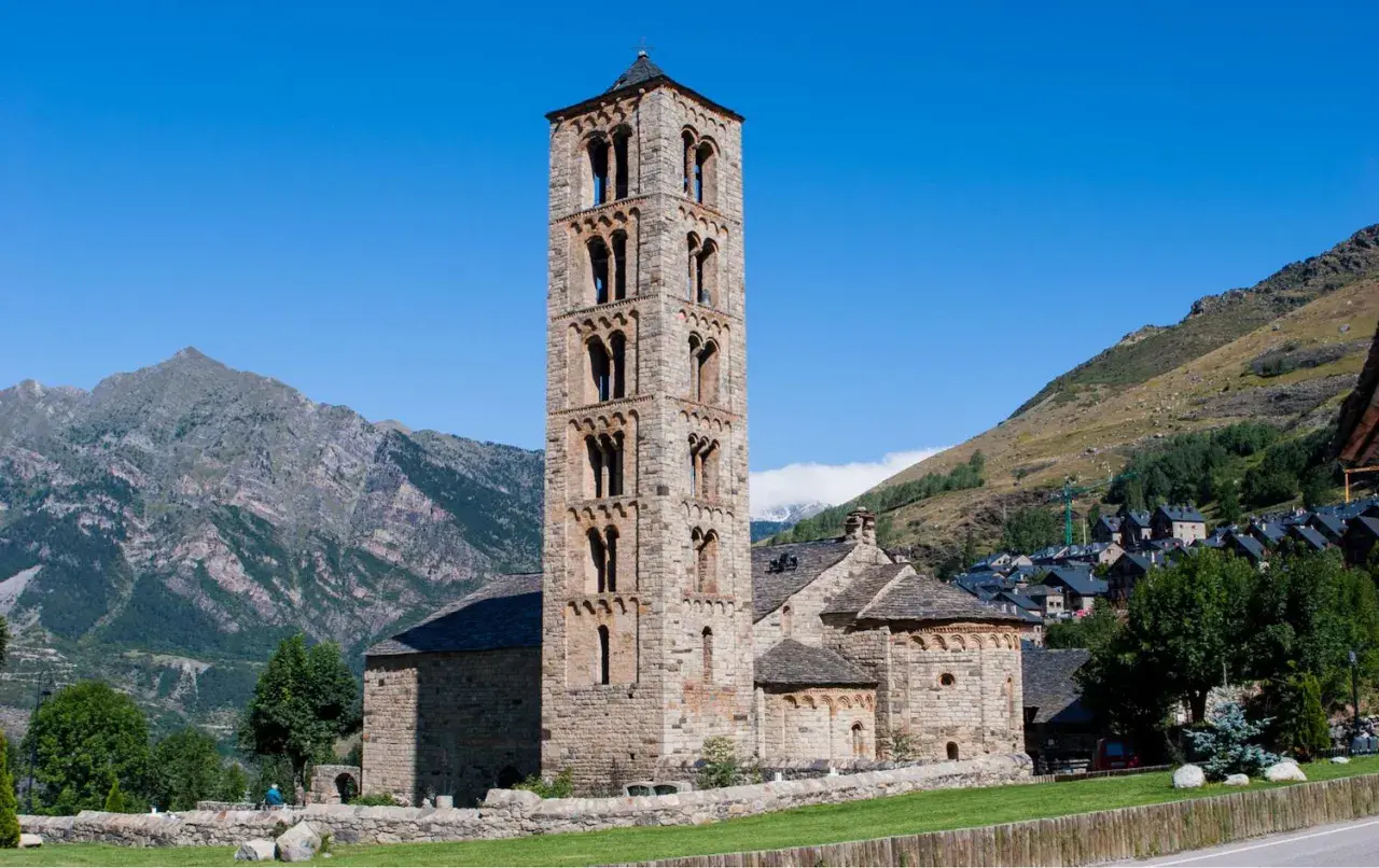 Torre románica de piedra en el Vall de Boí, con montañas y un pueblo al fondo.