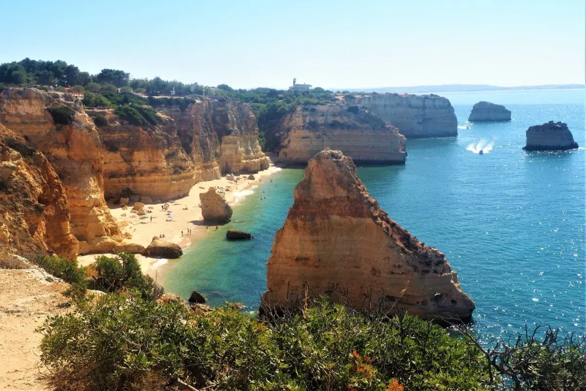 Acantilados dorados y aguas turquesas en una **playa** del **Algarve**. Gente disfrutando del sol y el mar.