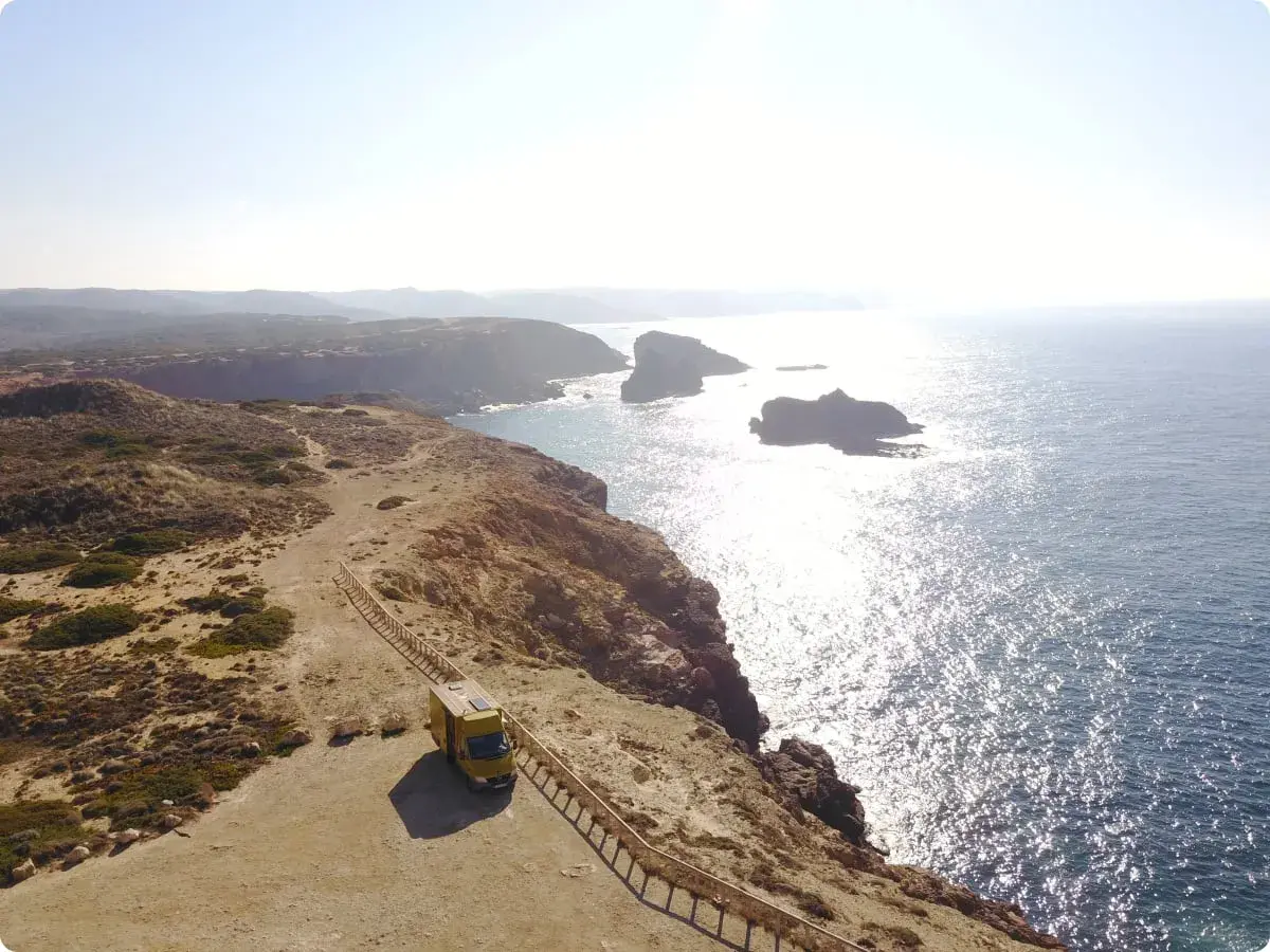 Furgoneta amarilla en un acantilado con vistas al mar, ideal para camping en Algarve, Portugal.