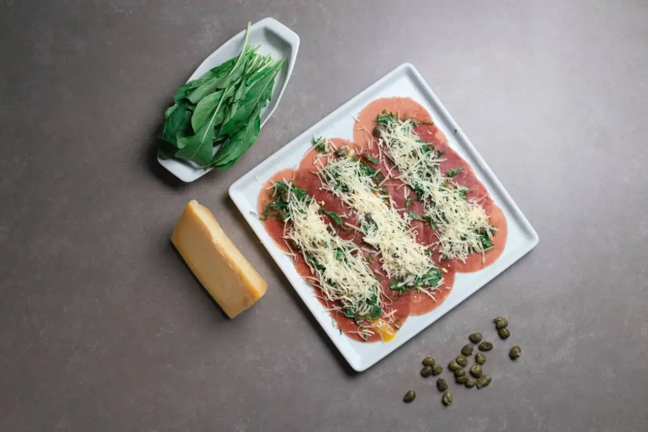 Carpaccio con rúcula y queso rallado, perfecto para llevar en autocaravana. Acompañado de un trozo de queso y alcaparras.