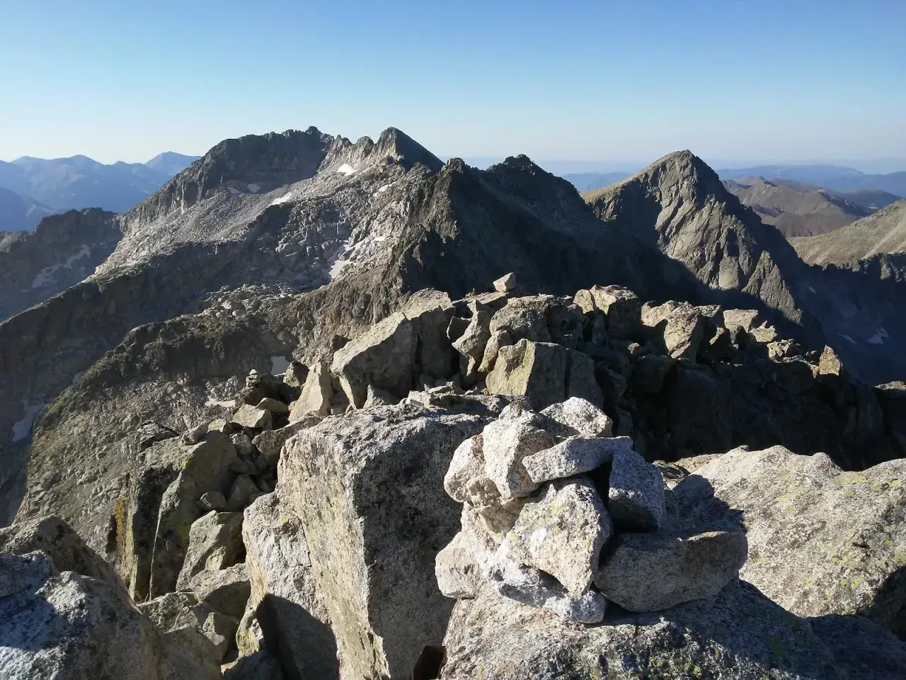 Cumbre rocosa con cairn, vista panorámica de montañas escarpadas bajo cielo azul. Besiberri Nord.