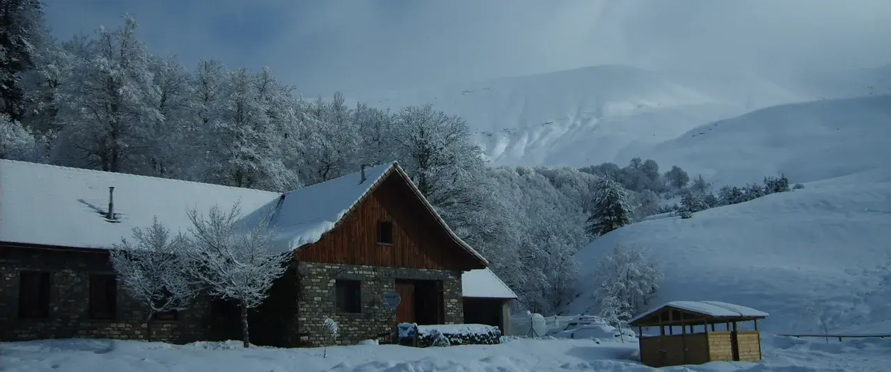 El refugio de Linza, cubierto de nieve, se alza entre árboles nevados y montañas imponentes.