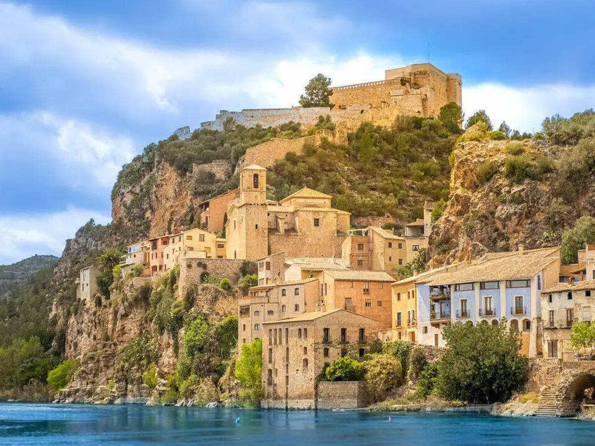 Pueblo de cambrils de muntanya aferrat a un penya-segat rocós, amb cases de colors i un castell imponent al cim.