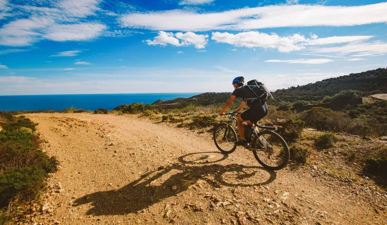 Ciclista disfruta de rutas en bici con encanto por la costa mediterránea. El mar azul y el cielo despejado acompañan su aventura.