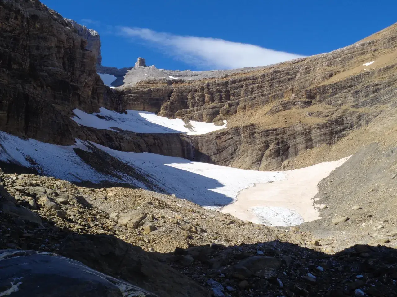 Un paisaje montañoso con nieve y rocas, donde el sol ilumina la **col de tentes** y el cielo azul.