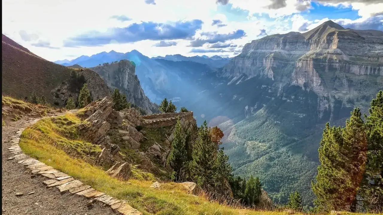 Sendero de piedra serpentea por la ladera con vistas a un profundo valle en los Pirineos de Huesca.