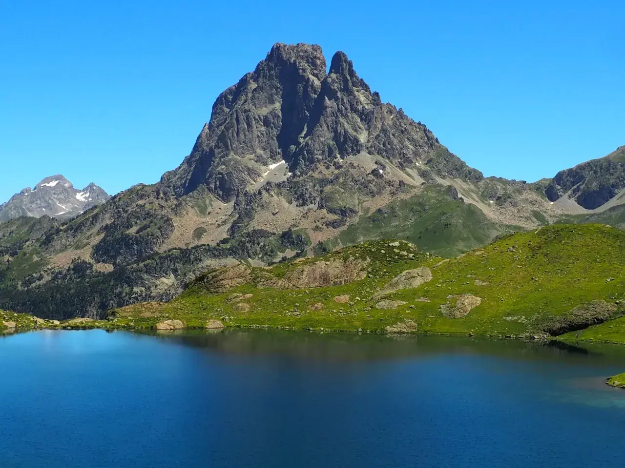 Lago azul intenso reflejando picos rocosos y verdes laderas en los Pirineos Francia.