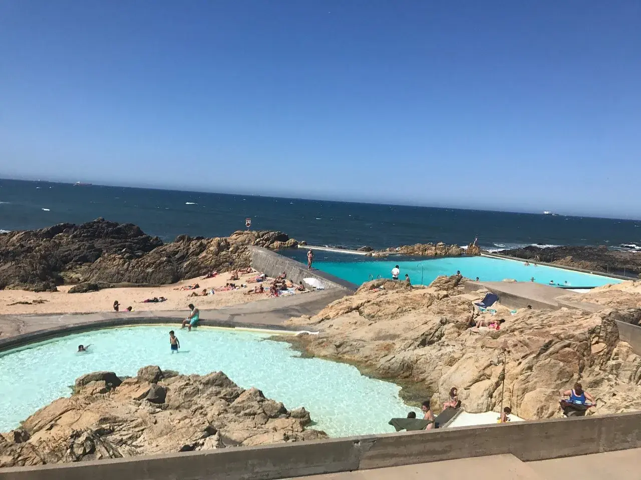 Piscinas naturais na praia de Matosinhos, Porto, com pessoas a nadar e a apanhar sol.