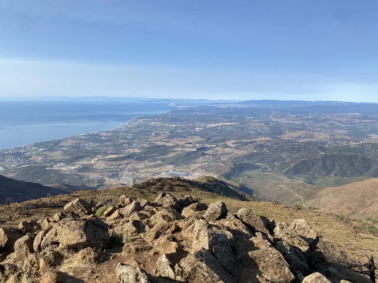 Vista panorámica desde la sierra bermeja, con el mar azul al fondo y un paisaje árido y rocoso en primer plano.