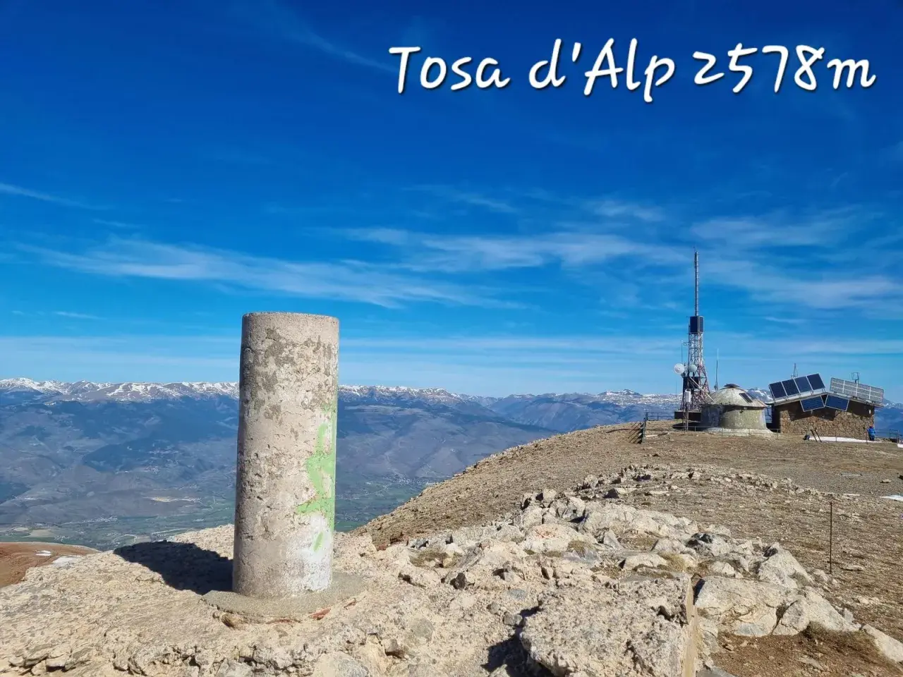 Cima de Tosa d'Alp, 2578m. Pilar de hormigón y antena de telecomunicaciones en un día soleado con vistas a montañas nevadas.