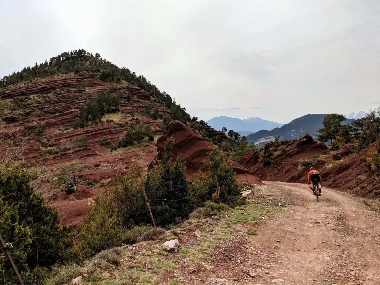 Ciclista en un camino de tierra rojiza, explorando las impresionantes rutas en bici Catalunya. Paisaje montañoso con formaciones rocosas únicas.