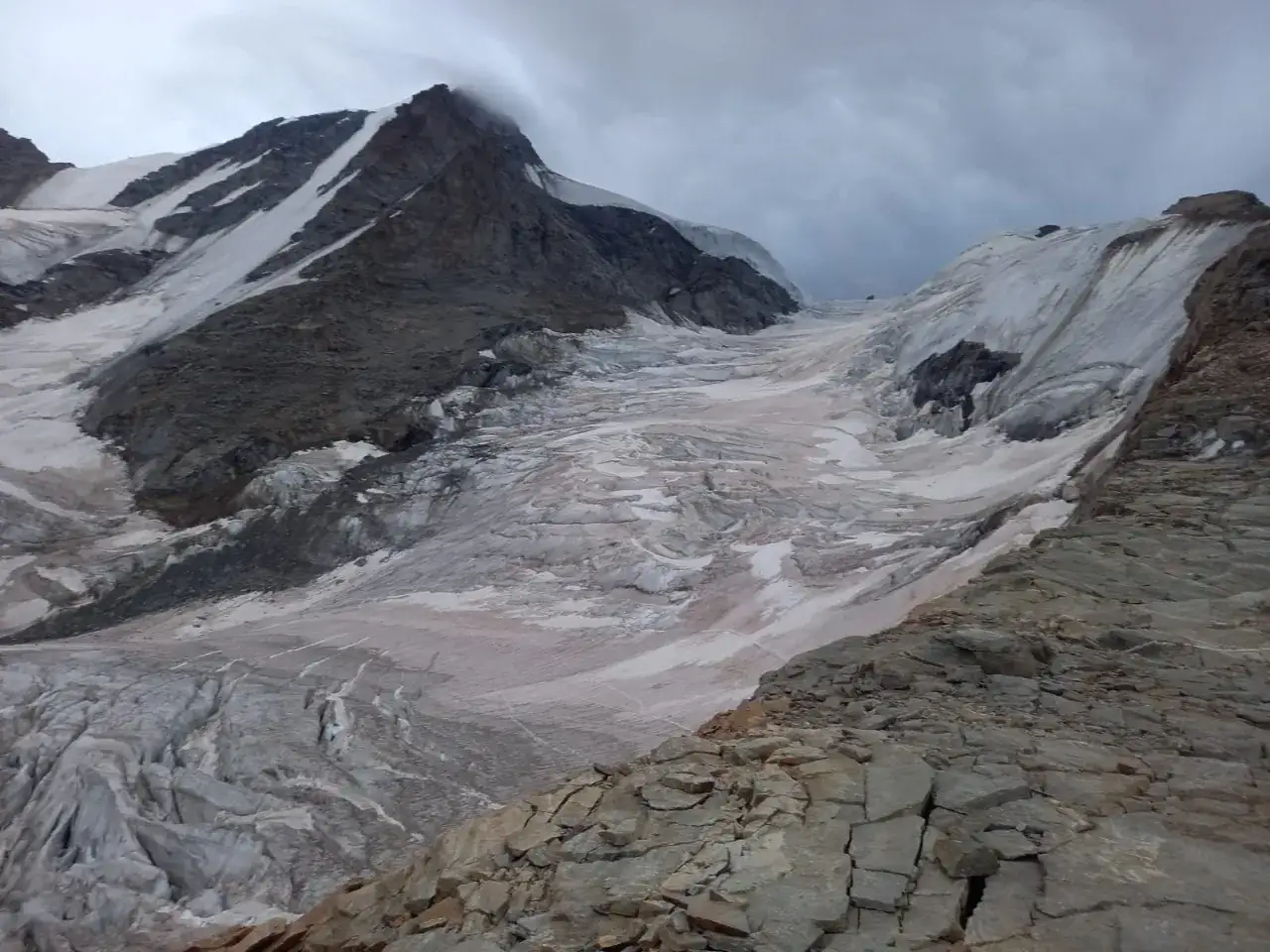 Un glaciar imponente desciende por las laderas rocosas de una montaña, un verdadero gran paradiso de hielo y piedra bajo un cielo nublado.