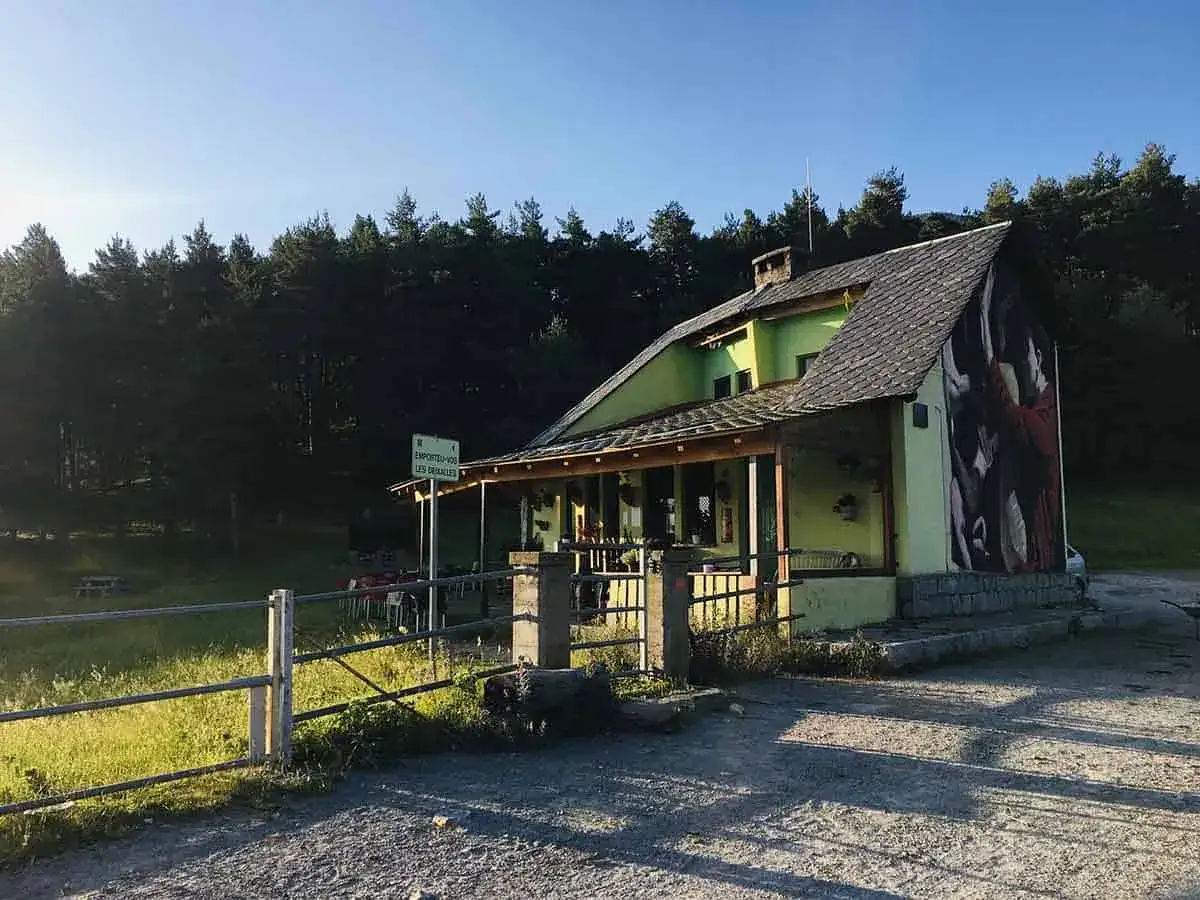El refugi Serrat de les Esposes, con su fachada verde y mural artístico, se alza entre pinos. Un cartel indica la entrada.