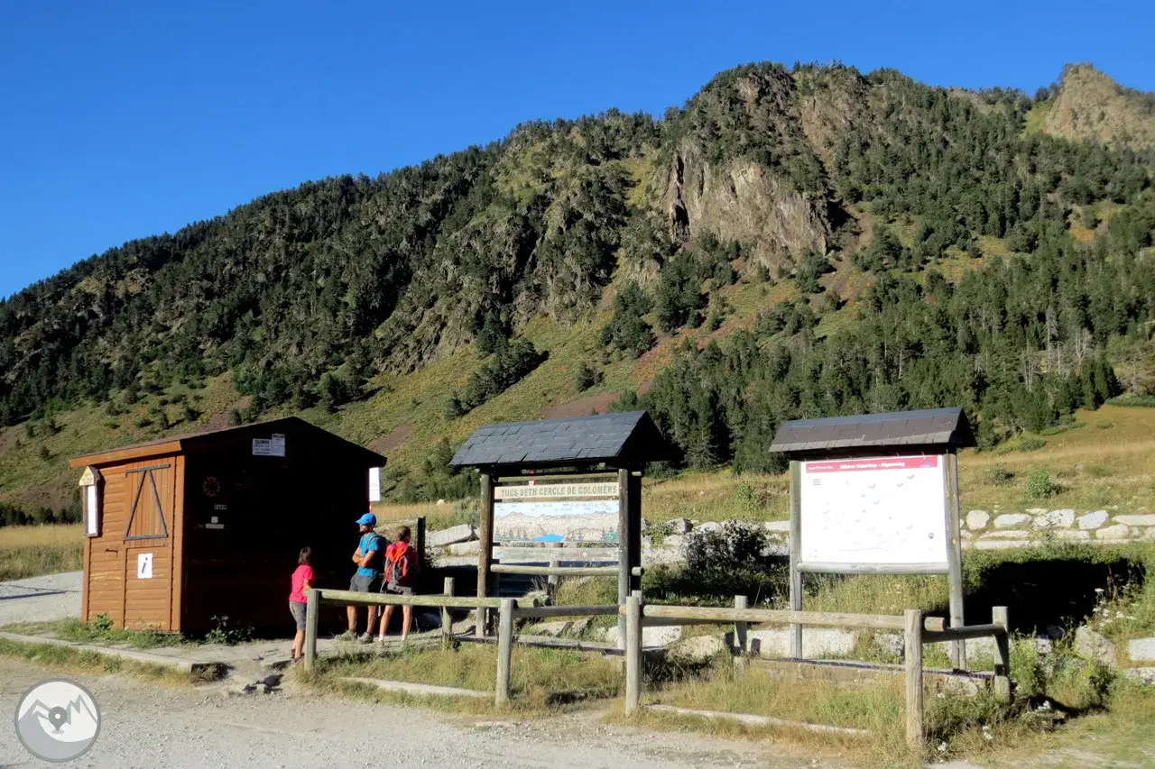 Pequeña caseta de madera junto a un cartel informativo, con una montaña boscosa al fondo. El refugio de Baiau parece ser el punto de partida.