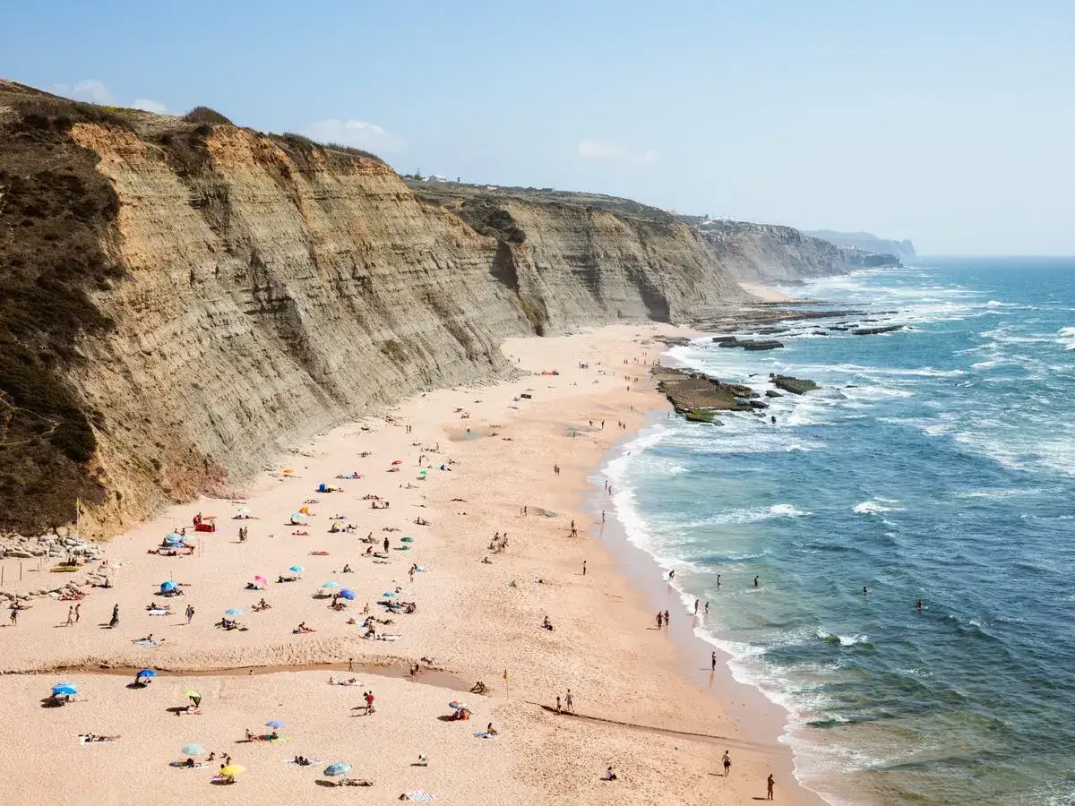 Amplia vista de las playas de Portugal con acantilados, arena dorada, gente disfrutando del sol y el mar azul con olas.