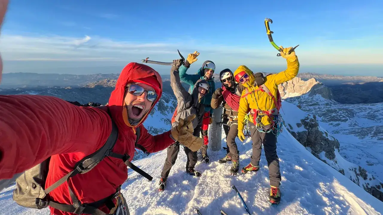 Grupo celebrando en la cima nevada, con piolets y equipo de alpinismo. ¡Éxito en sus cursos alpinismo!
