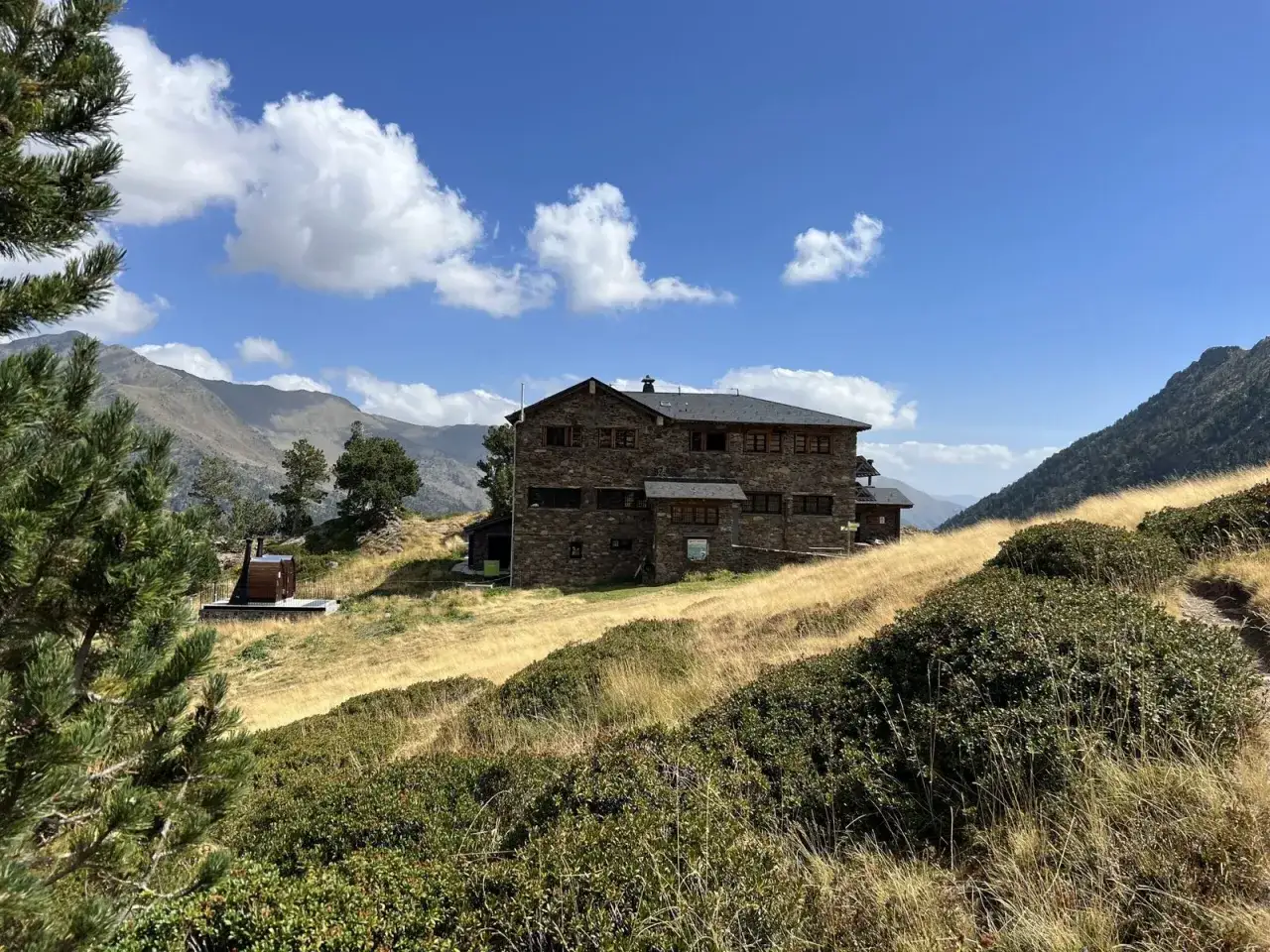 Edificio de piedra del refugio Comapedrosa en un día soleado con cielo azul y nubes blancas.