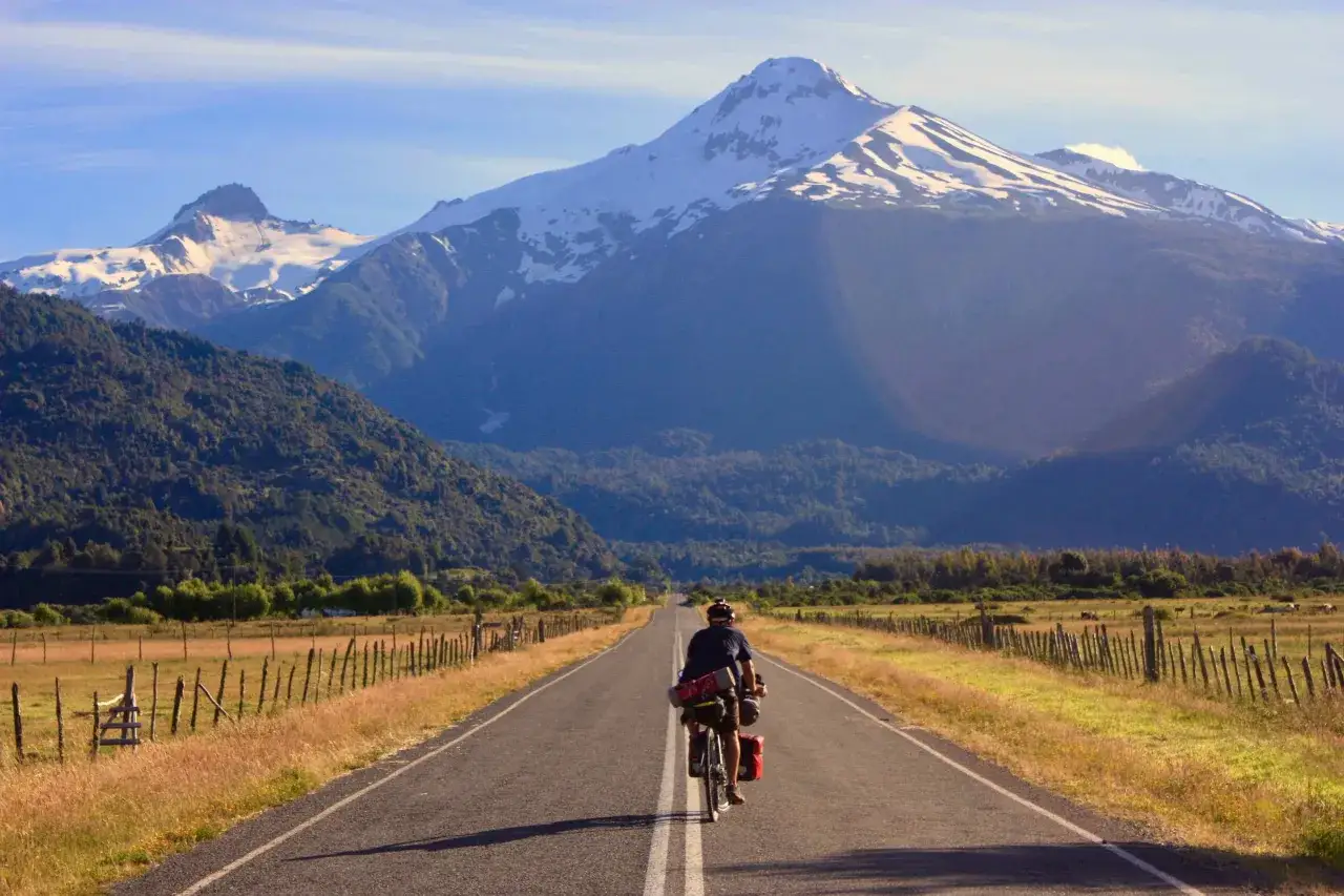 Ciclista pedaleando por la Carretera Austral, con imponentes montañas nevadas de fondo.