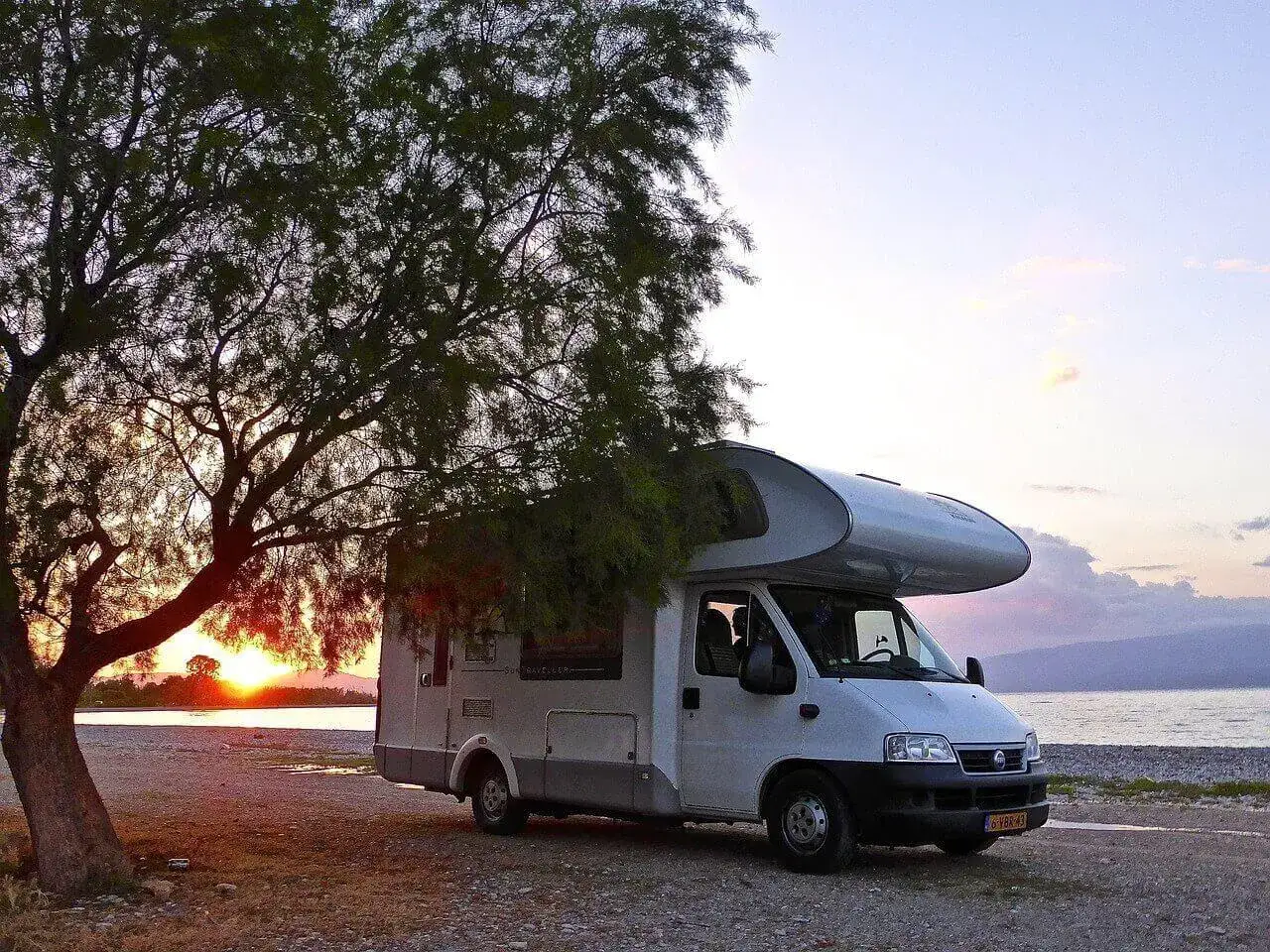 Autocaravana aparcada junto al mar al atardecer. Una aplicación para caravanas te ayudaría a encontrar lugares así.