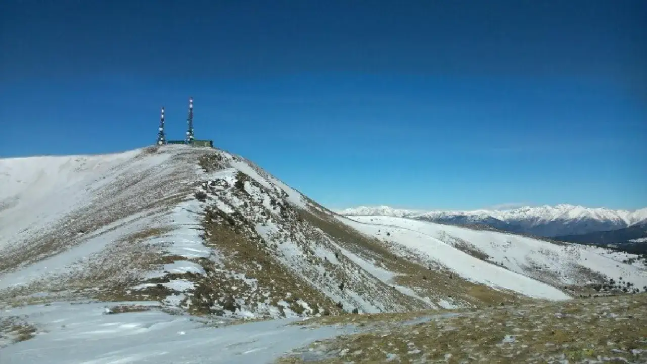 Cima nevada con una torreta de l orri y antenas, bajo un cielo azul intenso.