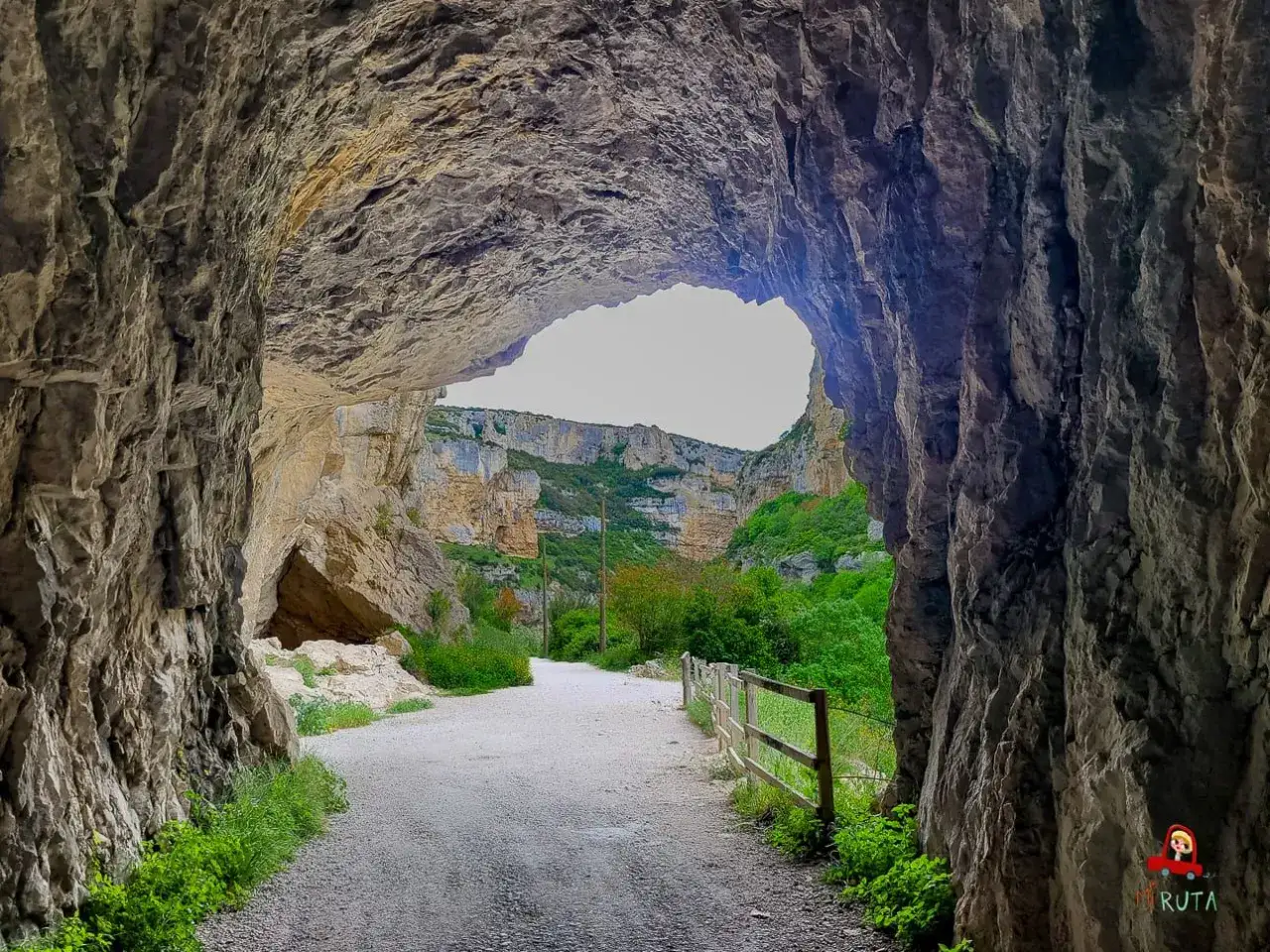 Salida de un túnel natural en la Foz de Lumbier, con un camino de grava que se adentra en un cañón verde y rocoso.