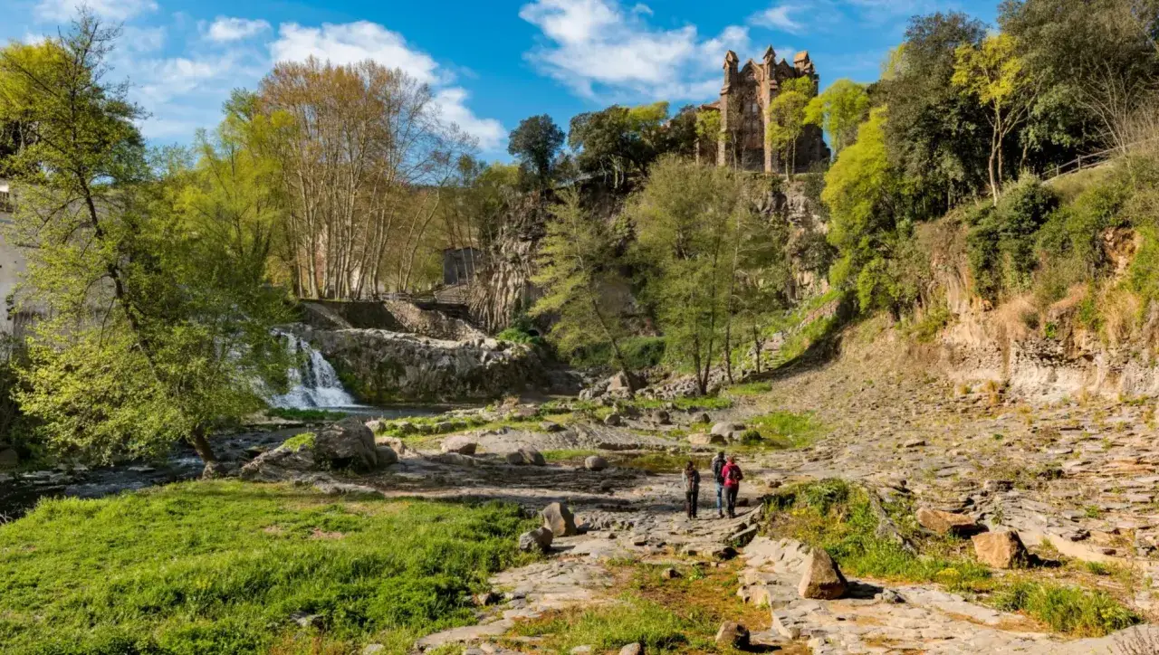 Senderos entre los volcanes de la Garrotxa, con un castillo en ruinas sobre un acantilado y una cascada.