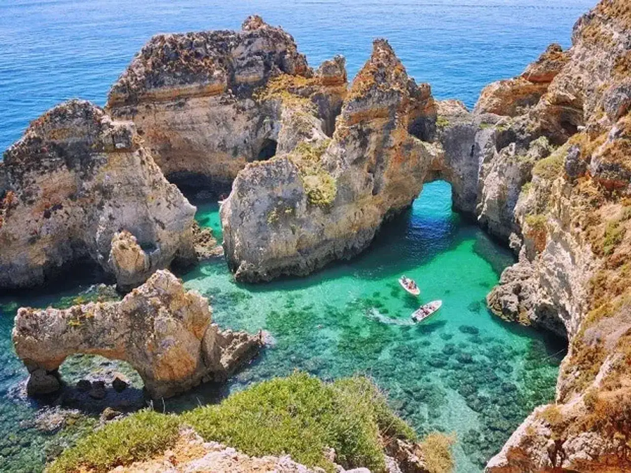 Aguas turquesas y formaciones rocosas espectaculares en una cala de la playa Algarve. Dos barcos exploran las cuevas marinas.