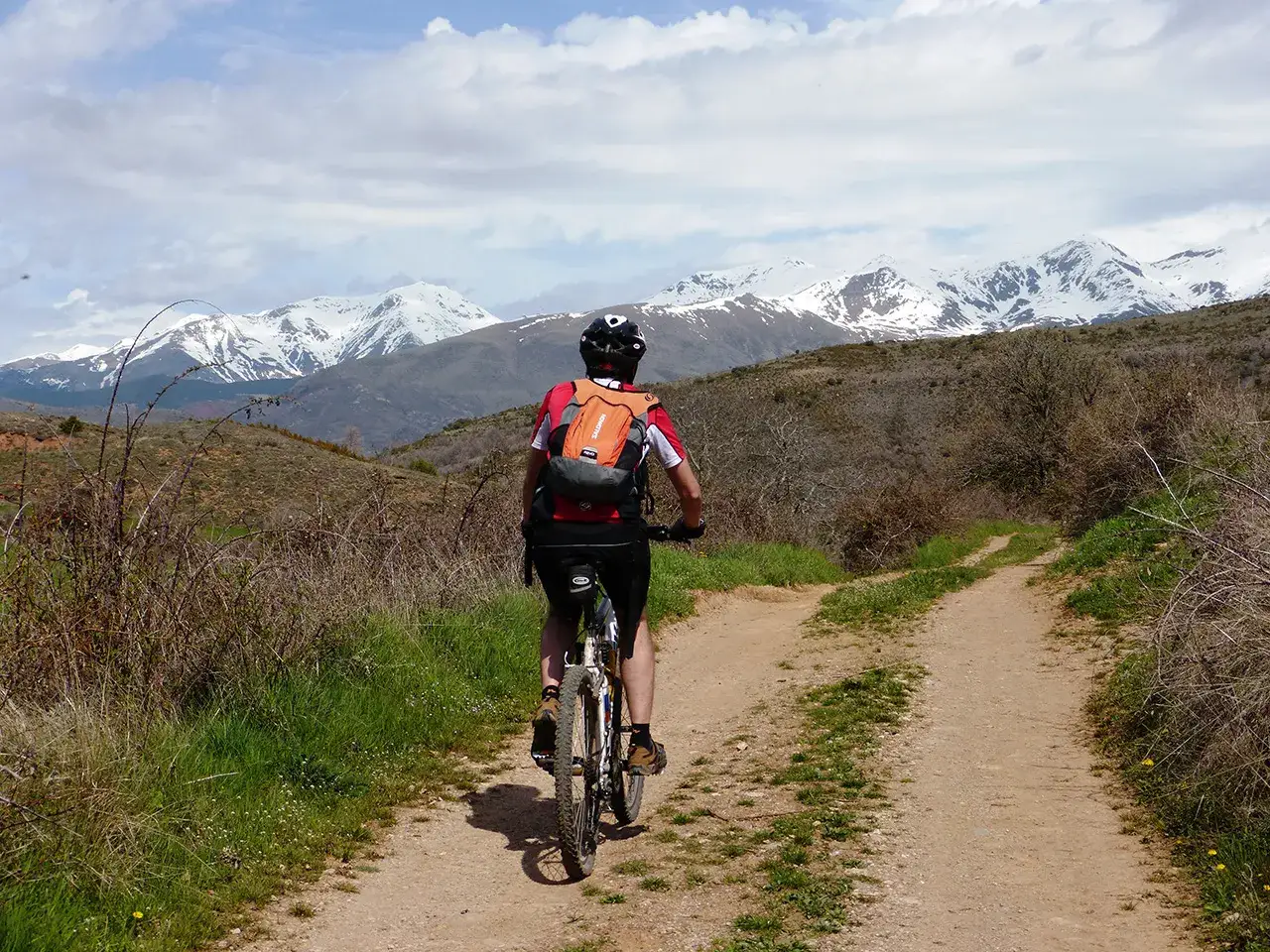 Ciclista pedalea por un sendero polvoriento, con la silueta de la geganta adormida, una montaña nevada, al fondo.
