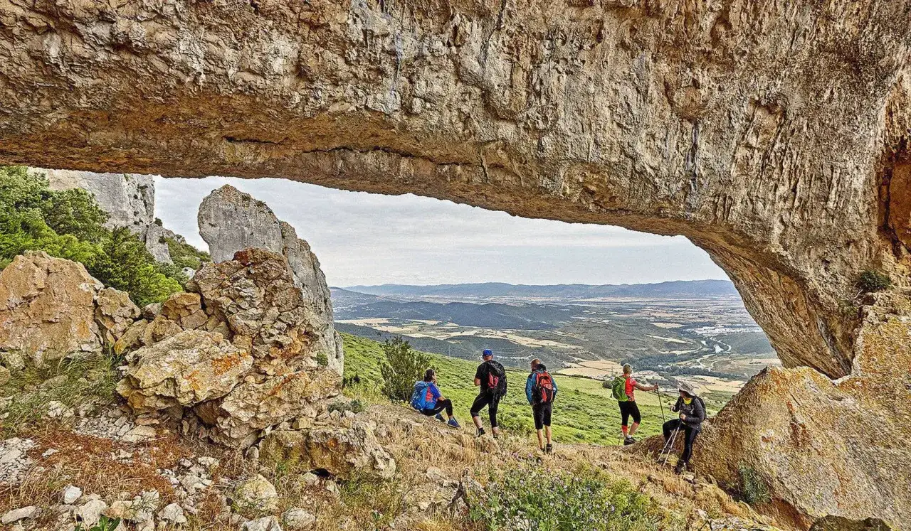 Senderos y rutas por Navarra bajo un arco natural de roca, con excursionistas admirando el paisaje.