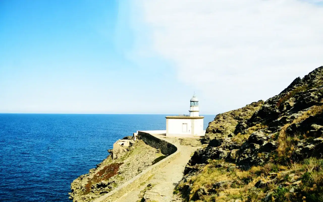 El faro de Cala Nans se alza sobre un acantilado rocoso, vigilando el azul intenso del mar Mediterráneo bajo un cielo despejado.