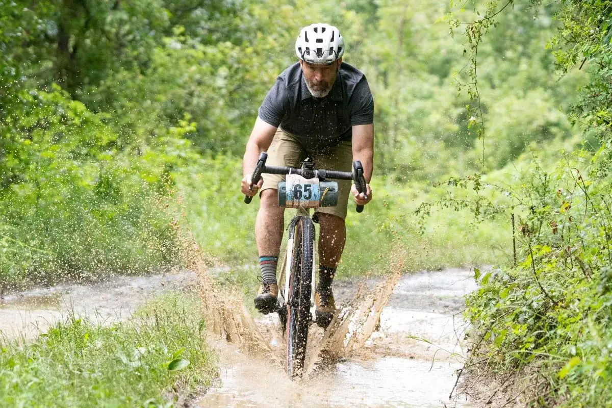 Ciclista con dorsal 65 atraviesa un charco de barro en una ruta de gravel transpirenaica.