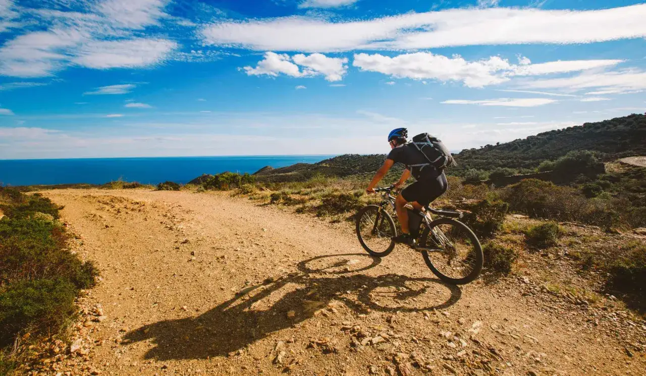 Ciclista pedaleando por senderos de tierra con vistas al mar. Perfectas rutas bicicleta para disfrutar del paisaje.