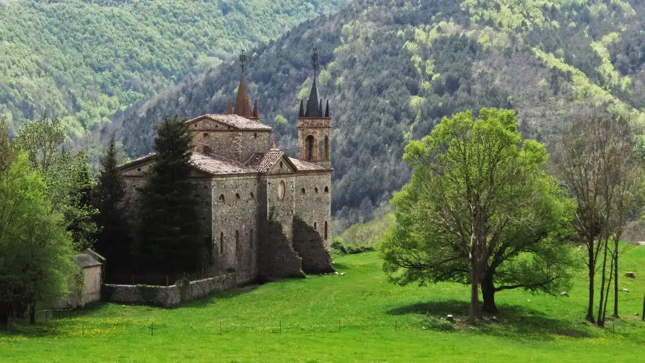 Edificio de piedra con torres y tejados rojos, rodeado de verde. Ideal para rutas Camprodon.
