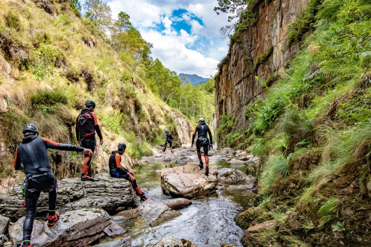 Grupo de personas con trajes de neopreno realizando actividades de montaña en un cañón rocoso con un río.