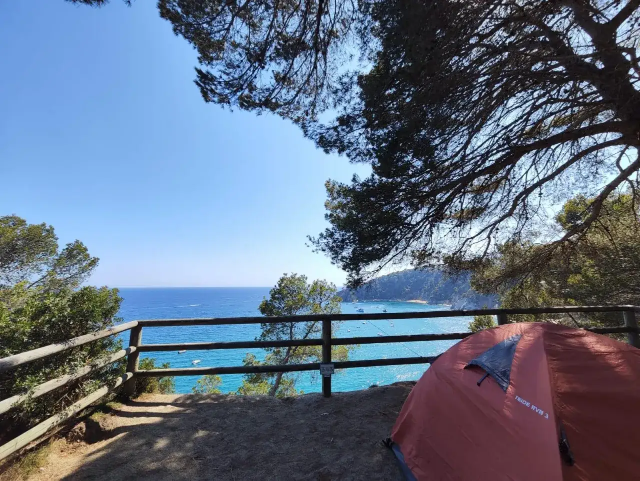 Tienda de campaña lista para disfrutar del camping en Portugal, con vistas al mar azul y barcos anclados.