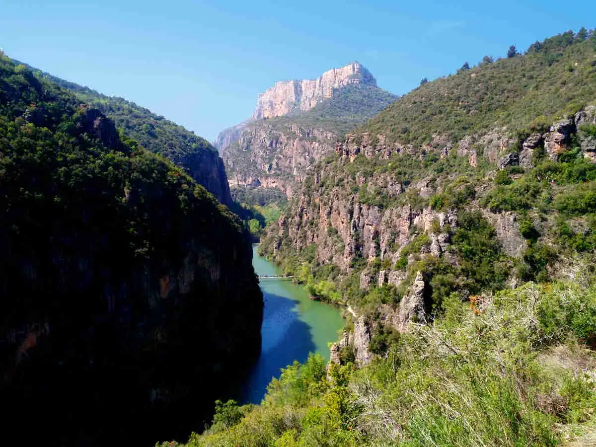 El río serpentea entre imponentes paredes rocosas en el congost del Mu, con vegetación cubriendo las laderas y un pico montañoso al fondo.