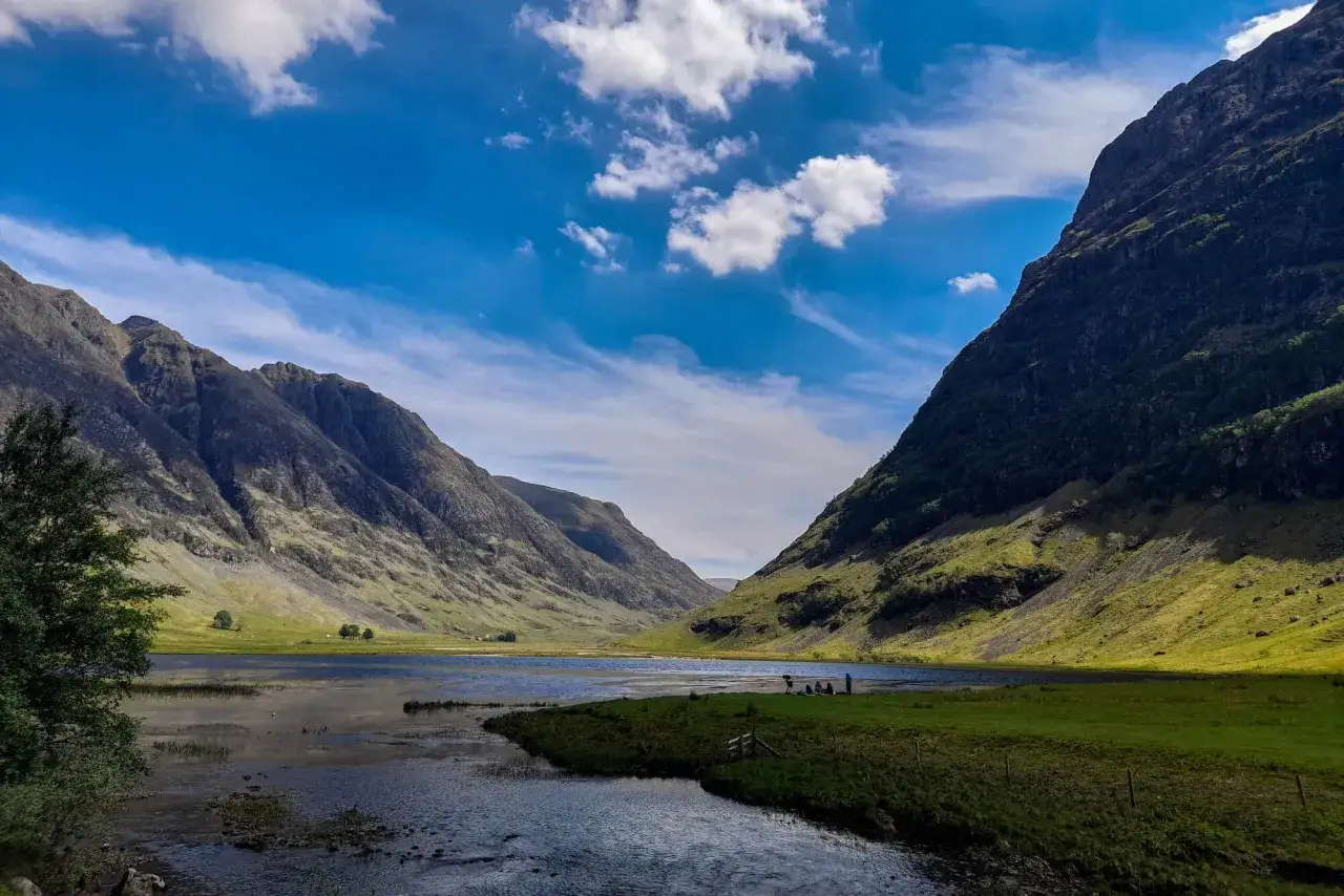 Un paisaje espectacular para hacer escocia en bicicleta. Montañas verdes, un lago sereno y cielo azul con nubes.