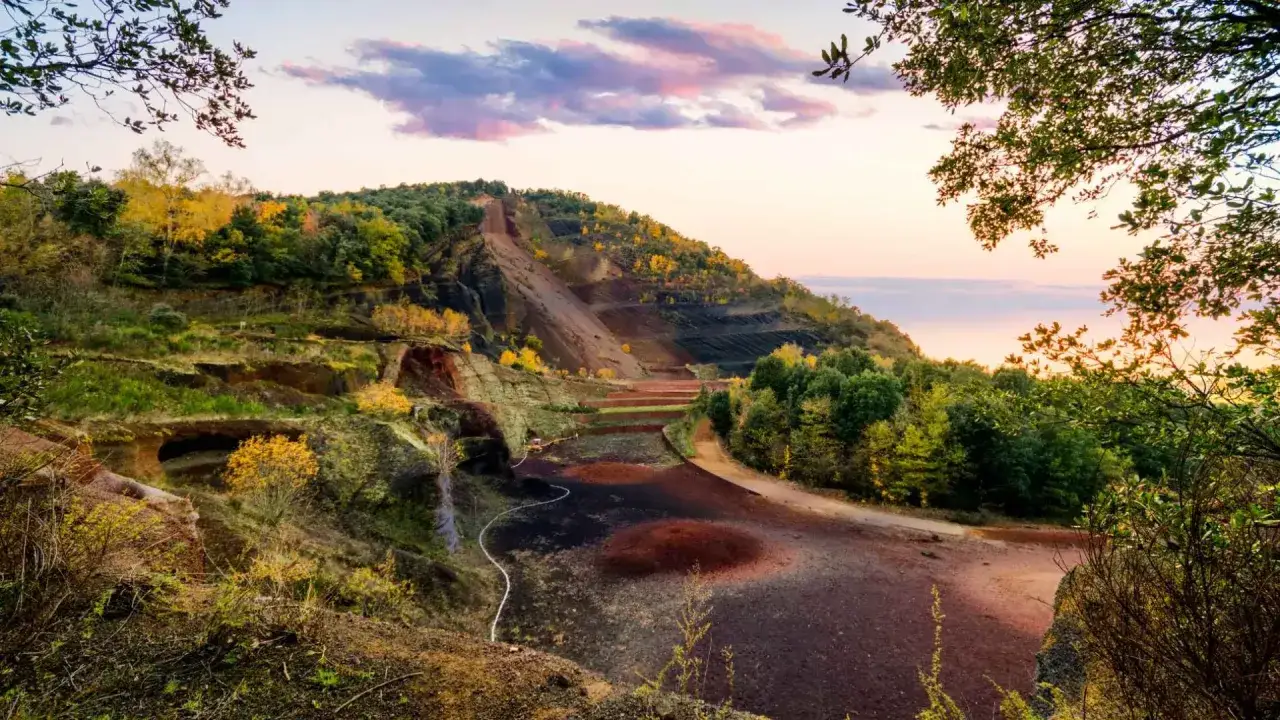 Paisaje volcánico en La Garrotxa con tonos ocres y verdes, terrazas y vegetación otoñal bajo un cielo rosado.