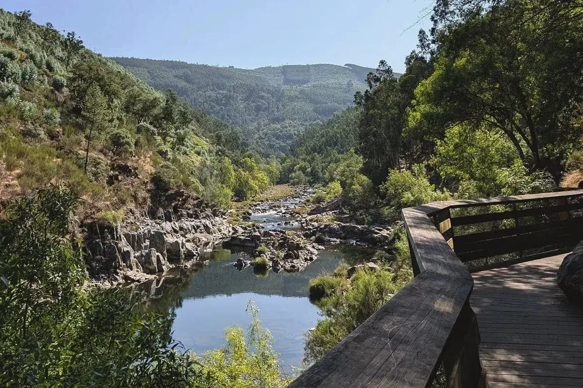 Pasarela de madera para senderismo Portugal, junto a un río rocoso y rodeado de vegetación exuberante.