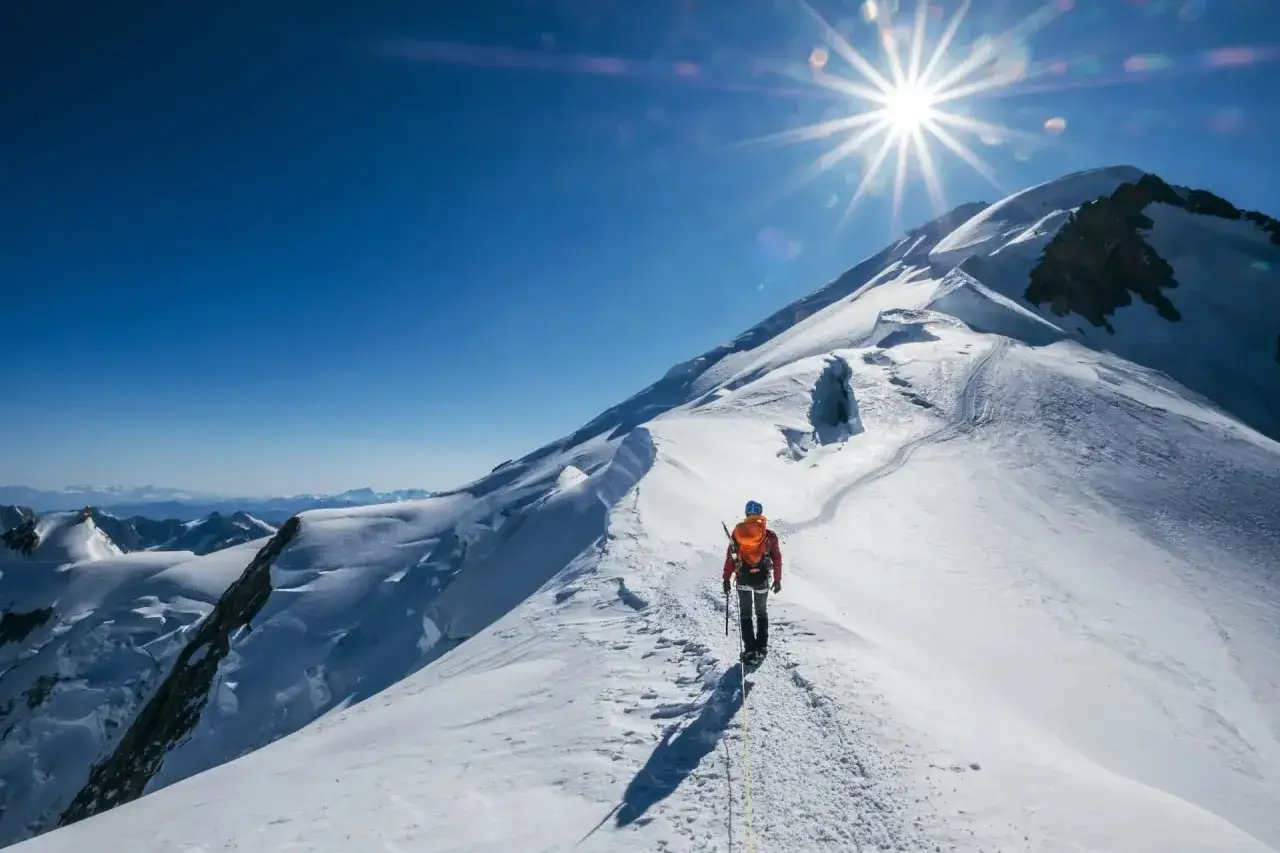 Alpinista solitario en la cresta nevada, con el sol brillando sobre el Mont Blanc. El camino para subir al Mont Blanc es desafiante pero gratificante.