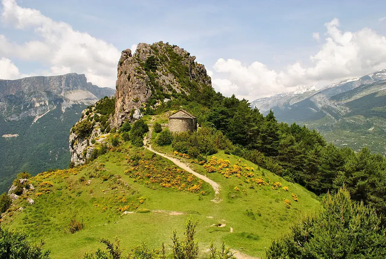 Las ermitas de Tella, pequeñas joyas de piedra, se alzan en un paisaje montañoso verde y florido, con un camino serpenteante que invita a la contemplación.