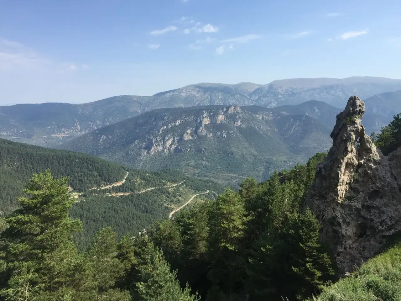 Vista panorámica de la muntanya d'Alinyà, con picos rocosos, bosques de pinos y una carretera serpenteante.