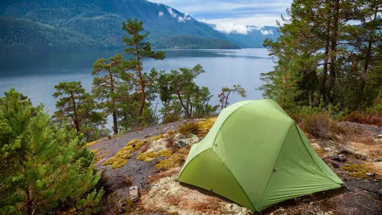 Tienda verde en un paisaje montañoso con un lago, ideal para acampada libre España.