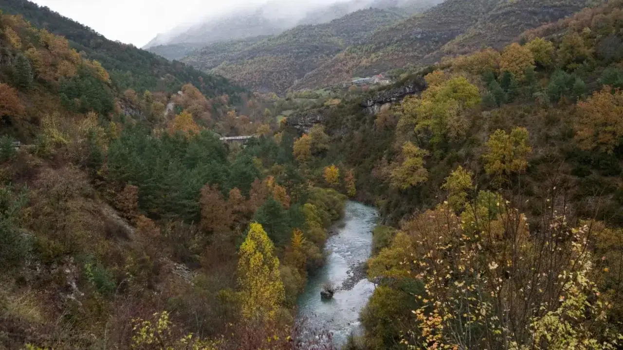 El valle de Ansó se despliega con un río serpenteante entre montañas cubiertas de bosques otoñales en tonos ocres y verdes.